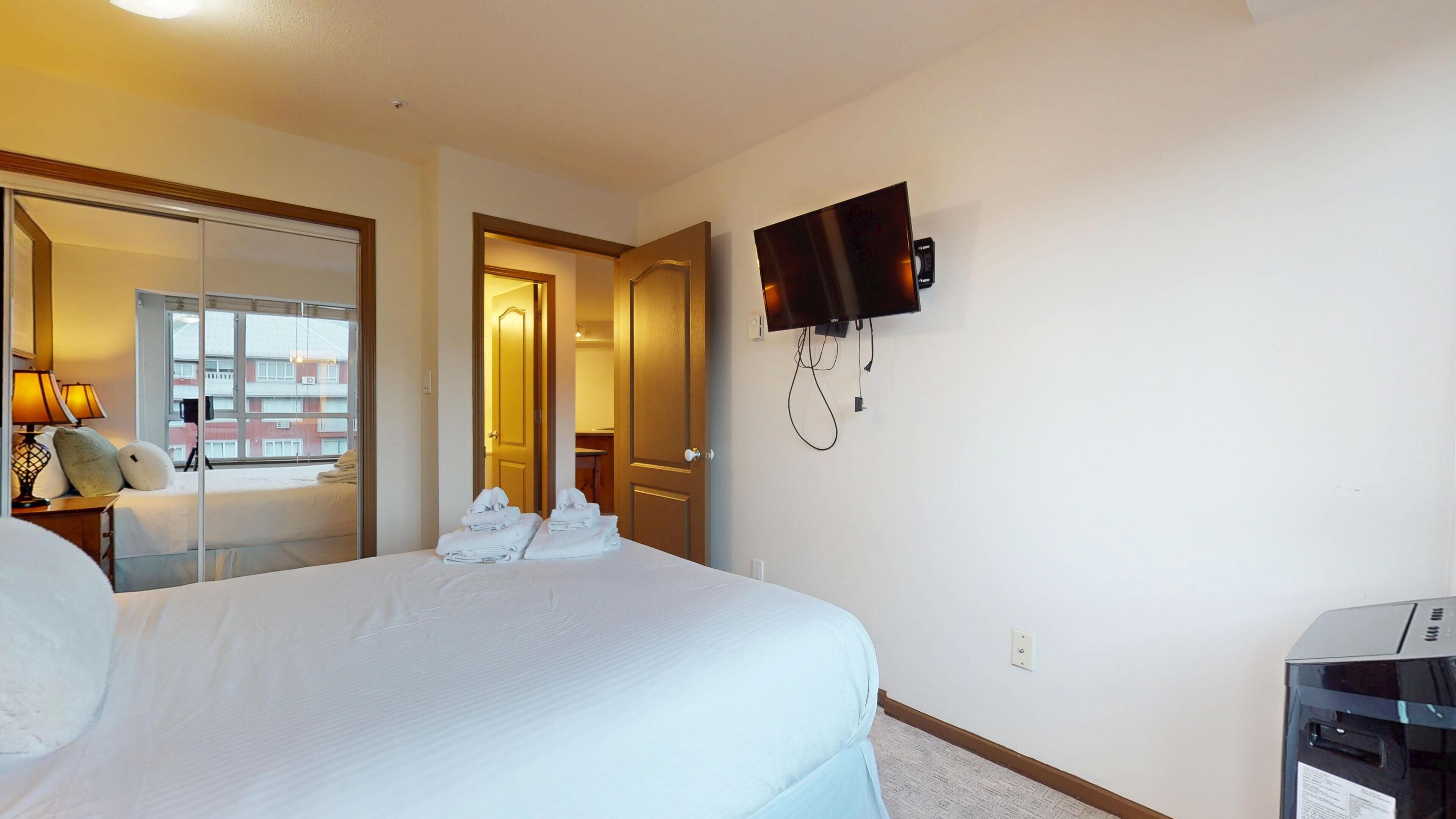 Une chambre d’hôtel avec un lit, un téléviseur fixé au mur et un bureau avec une lampe.