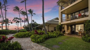 A modern hotel with a stone pathway leading to a covered outdoor seating area, surrounded by lush greenery and palm trees. - SUMMER REDUCED! Villa 115 Oceanfront Turtle Bay (Kahuku)