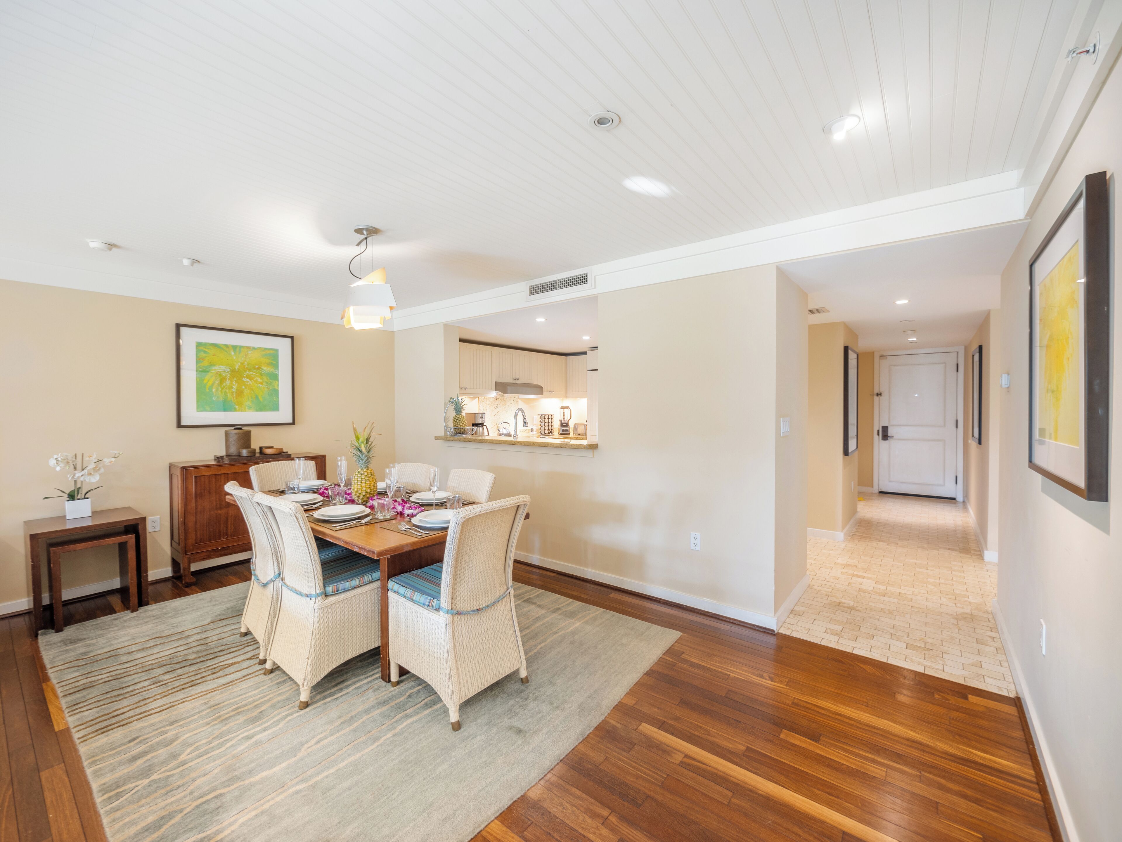 A dining area with a wooden table, two chairs, a rug, and a kitchen in the background.