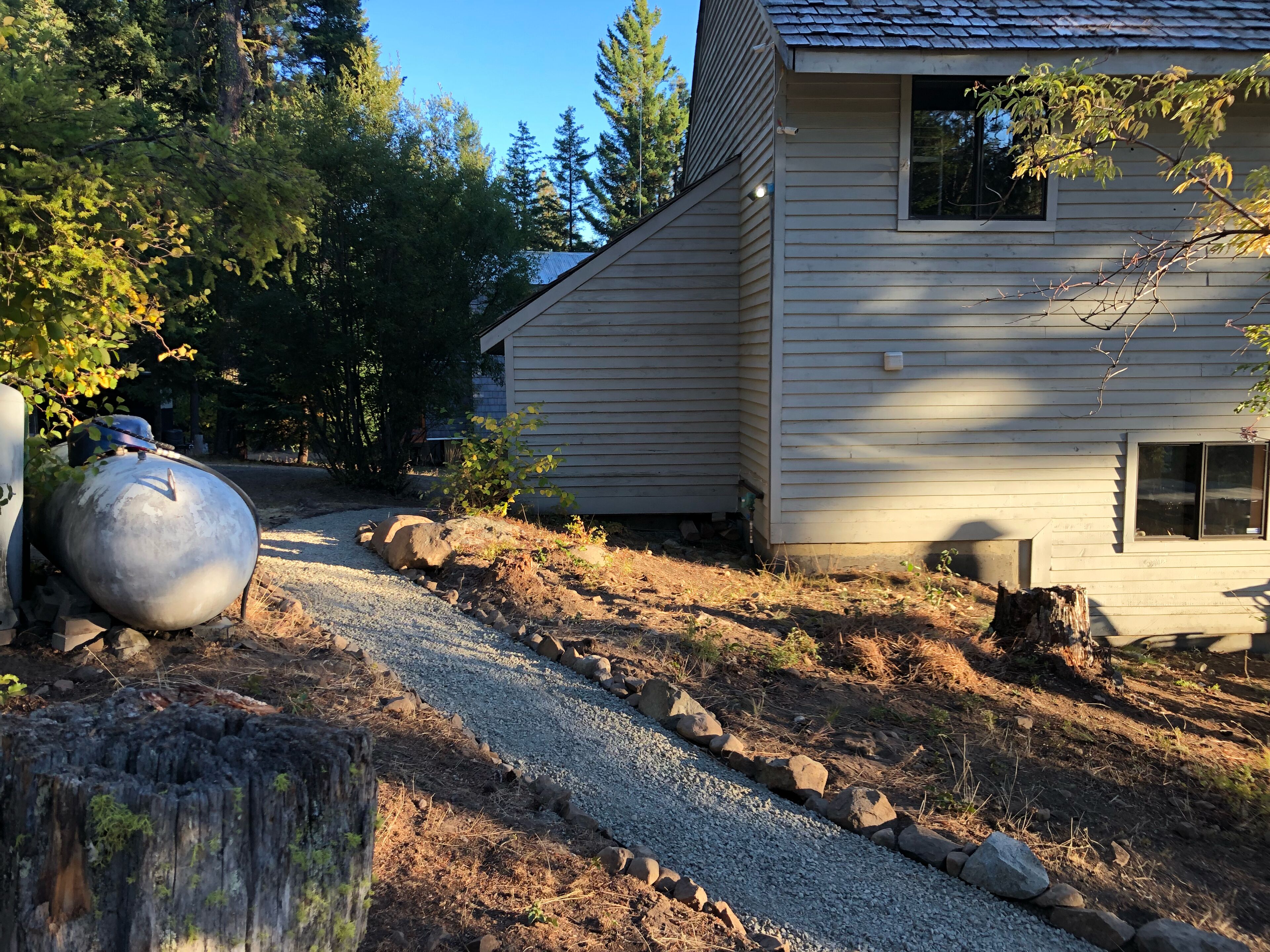 A house with a gravel driveway, a large water tank, and a wooden stump.