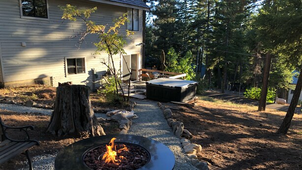 A backyard with a fire pit, a wooden deck, and a house.
