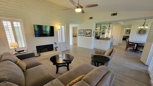 A spacious living room with a fireplace, a large flat-screen TV, and a ceiling fan. -  Desert Oasis, Golf, Stunning Southwest Mountain Views, Serene and Private! (Palm Desert)