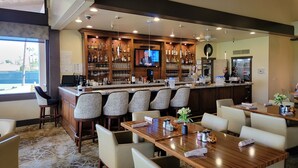 A bar area with a counter, bar stools, and a television screen. There are tables and chairs arranged for dining. -  Desert Oasis, Golf, Stunning Southwest Mountain Views, Serene and Private! (Palm Desert)