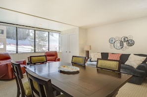 A dining area with a wooden table, red leather chairs, and a view of a snowy landscape through large windows. - True Ski-in/Out, Free WiFi & pkg, Sunroom, W/D, Steps to American Eagle lift (Copper Mountain)