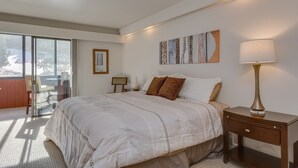 Una camera da letto con un letto grande, un comodino con una lampada, una sedia, una finestra che dà su alberi e un pannello decorativo al muro.