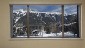 Una finestra con vista su montagne innevate, un parcheggio e degli edifici.