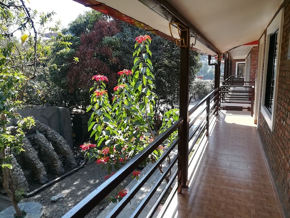 A balcony with a view of a garden, a brick wall, and a tiled floor.