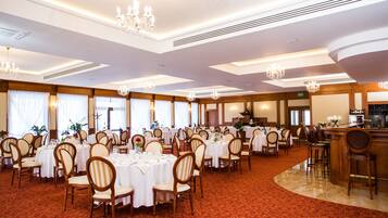 Un salón de banquetes con mesas redondas, sillas, candelabros y una zona de bar.