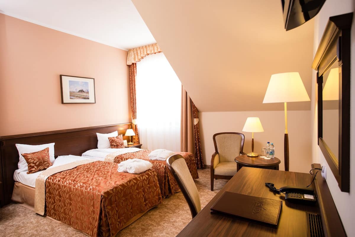 A hotel room with a bed, two bedside tables, a chair, a desk, and a lamp.