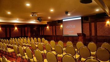 A conference room with rows of chairs, a podium, and a projection screen displaying "VENTUS".