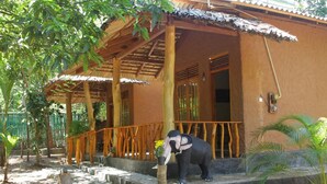 A building with a wooden porch, a statue of an elephant, and a small garden area with palm trees. - Peace Heaven (Udawalawa)