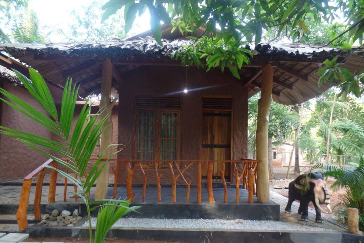A rustic building with a porch, a small elephant statue, and a palm tree.