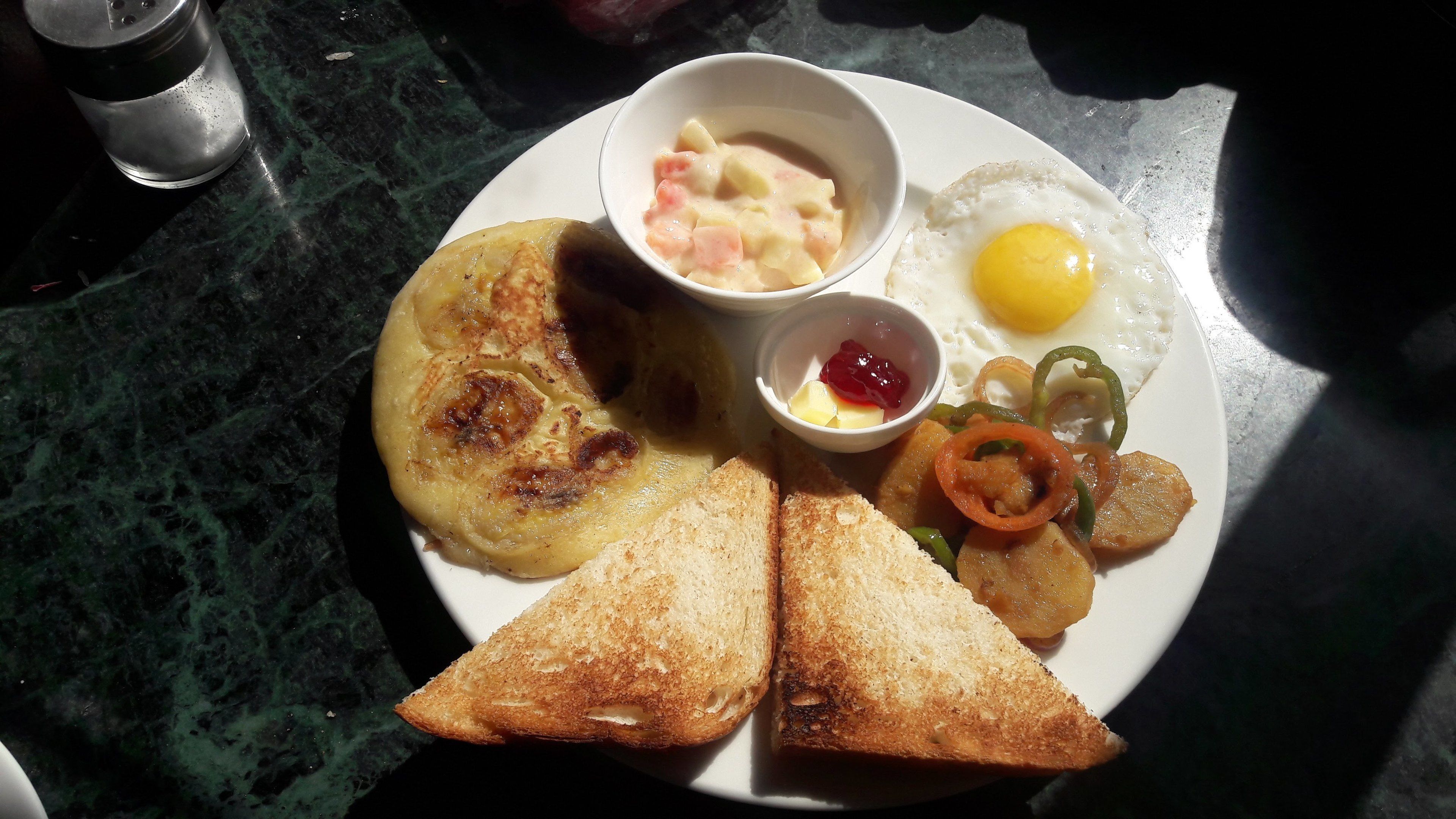 A plate with toast, fried egg, hash browns, and a small bowl of jam.