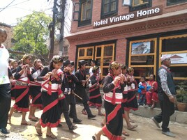 Un grupo de personas vestidas con atuendos tradicionales bailando frente a un edificio con un letrero que dice 'Hotel Vintage Home'.