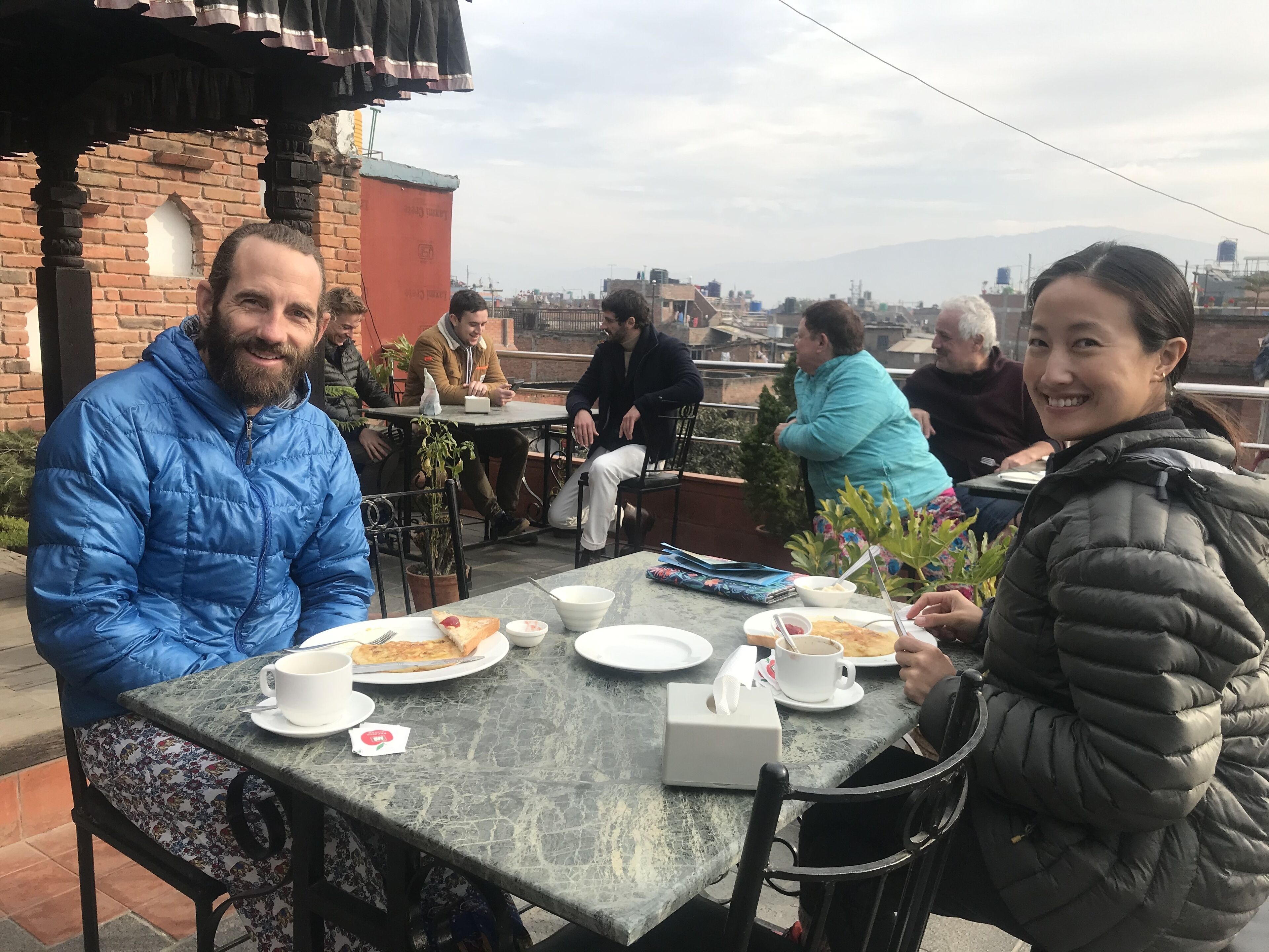 A group of people dining outdoors at a table with plates of food, cups, and a tissue box.