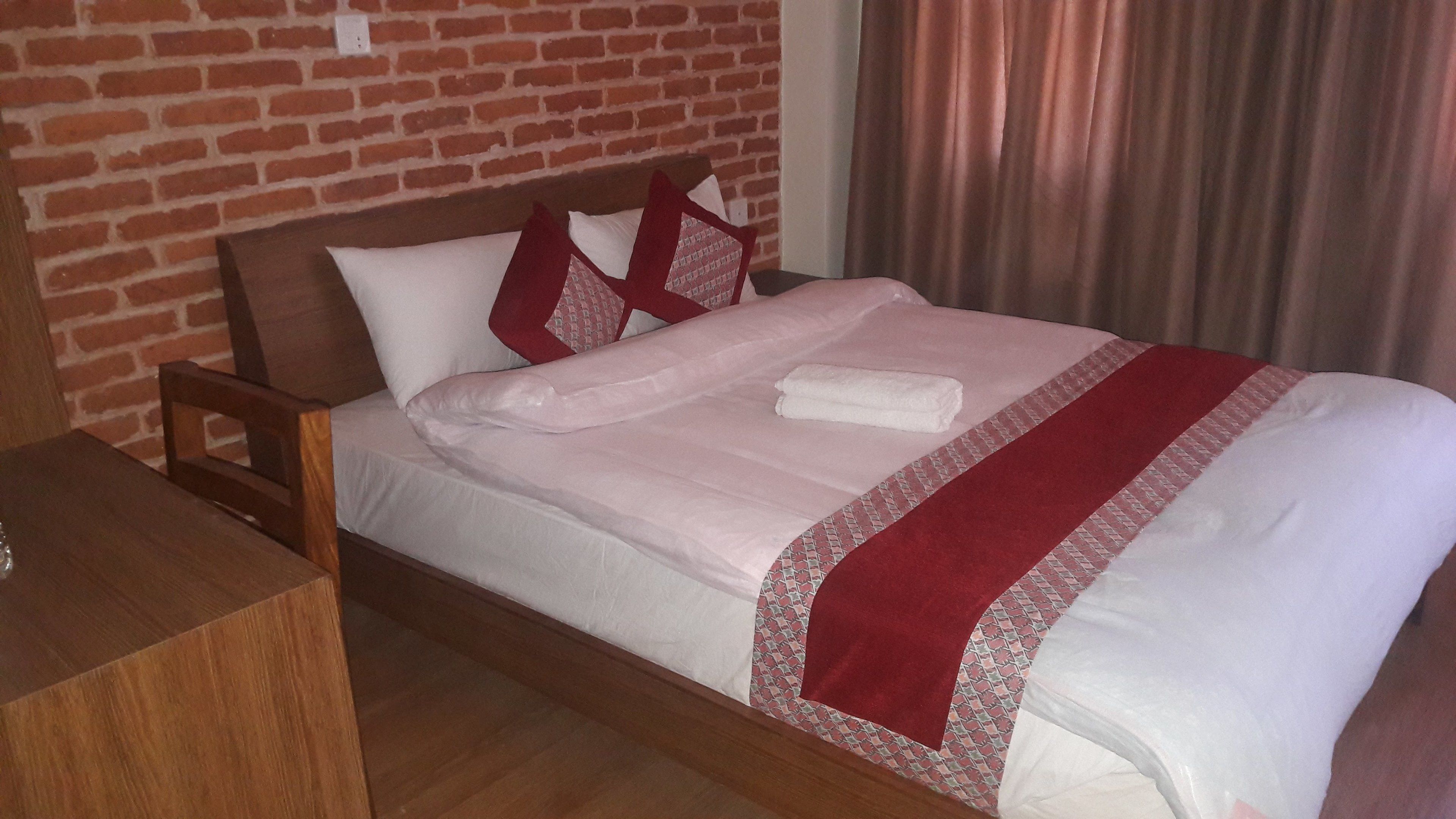 Een net opgemaakt bed met een rood-wit geboeide spreidekker, een houten hoofdbord en een nachtkastje van hout.