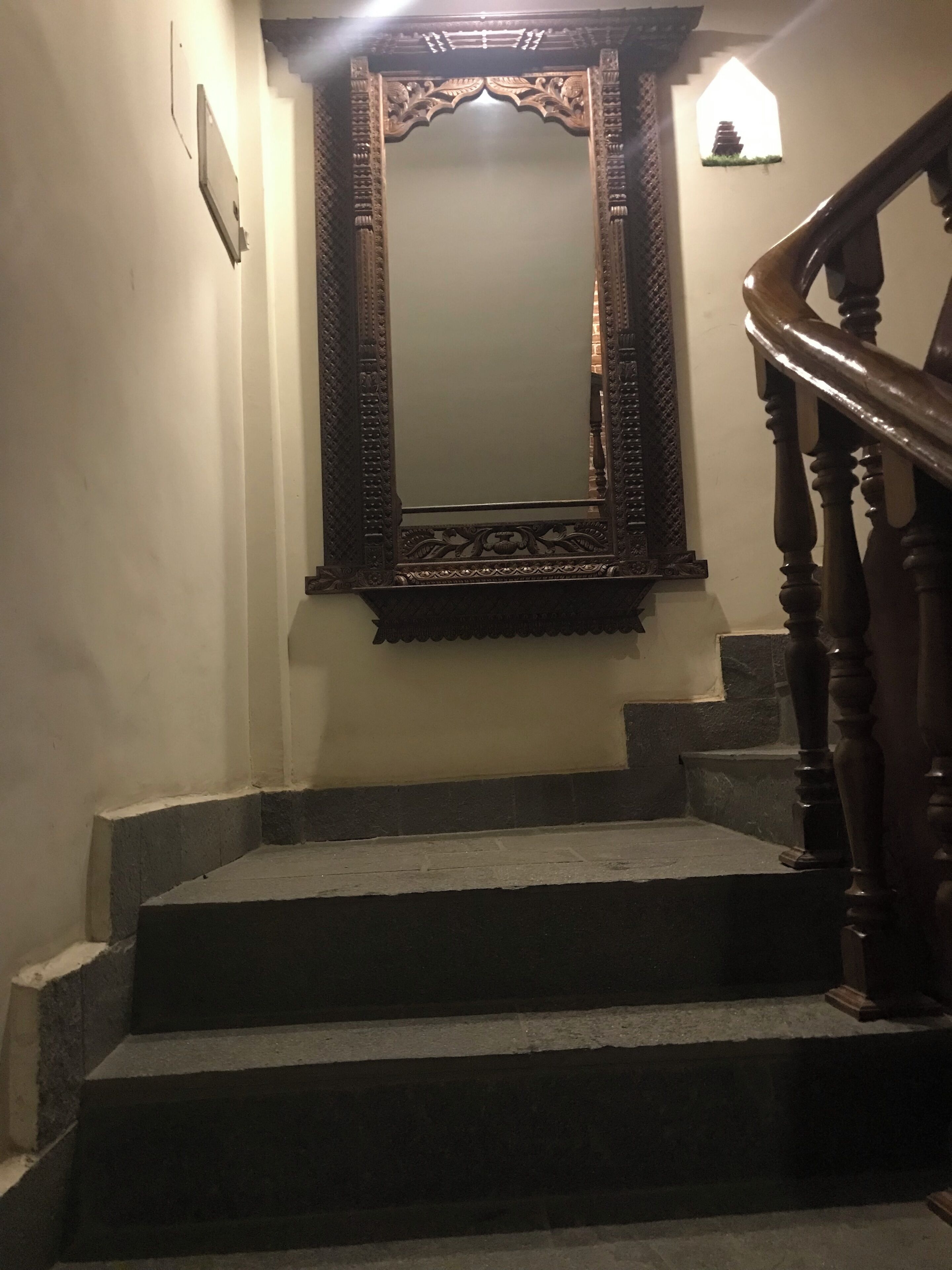 A staircase with a wooden handrail and a large ornate mirror above it.