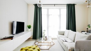 A modern living room with a flat-screen TV, a glass coffee table, a white sofa, and a green curtain. - Fantastay - Portokal Downtown Dubai (Dubai)