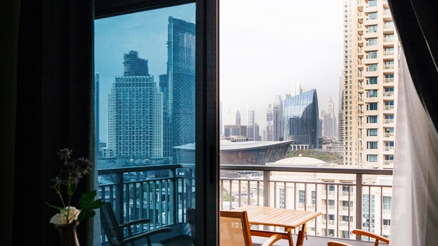 A balcony with a table and chairs, a vase with flowers, and a cityscape view through large windows. - Fantastay - Portokal Downtown Dubai (Dubai)