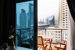 A balcony with a table and chairs, a vase with flowers, and a cityscape view through large windows. - Fantastay - Portokal Downtown Dubai (Dubai)
