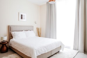 A neatly made bed with white linens, a bedside lamp, and a framed picture on the wall.