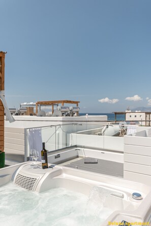 A hot tub with a bottle of wine and glasses, a pergola with lounge chairs, and a view of the sea. - Aphrodite luxury apartments (Naxos)