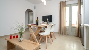 Zona menjador moderna amb taula de fusta i cadires blanques, una petita planta i una ampolla de vi.
