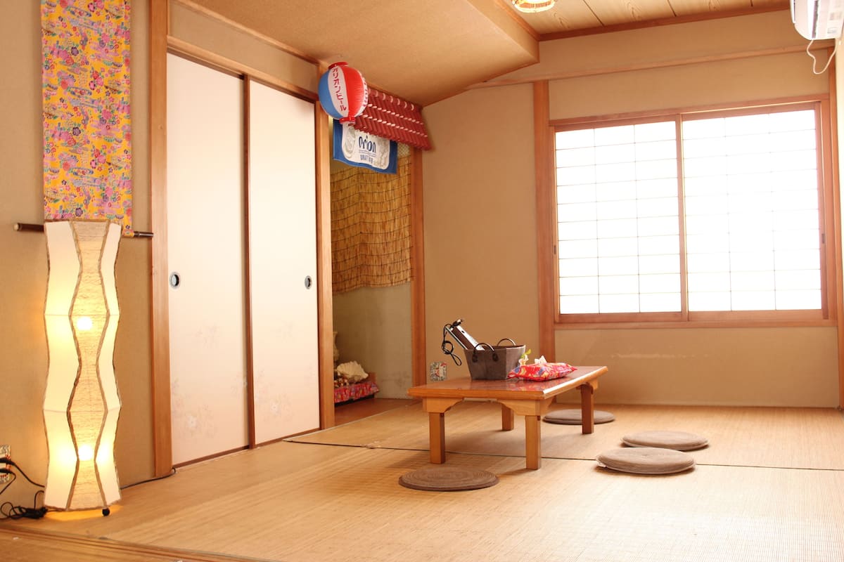 Une pièce de style japonais traditionnel, avec un sol recouvert de tatamis, un paravent shoji, un futon servant de lit, une petite table en bois et une lanterne décorative suspendue.