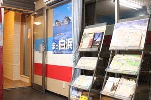 A hotel reception area with a glass door, a poster of a coastal scene, and a rack of brochures. - Seaside Pension Petit Shirahama (Shirahama)