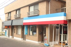 A building with a red, white, and blue awning, a visible entrance, and a bicycle parked outside. - Seaside Pension Petit Shirahama (Shirahama)