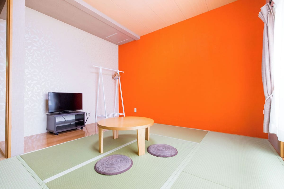 A room with a television, a small table, and a futon bed.