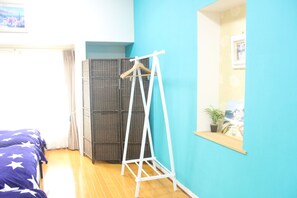 A room with a bed, a white clothes rack, a wicker wardrobe, and a window with a plant. - Seaside Pension Petit Shirahama (Shirahama)