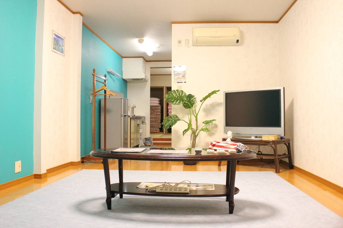 A room with a wooden table, a potted plant, a television, and a wardrobe.