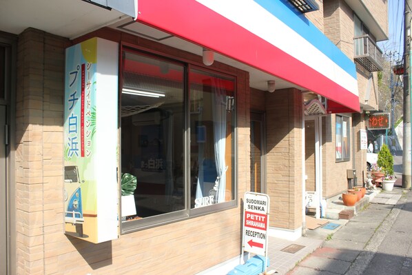 A building with a red awning, a sign for Sudomari Senka Petit Shirahama Reception, and a window with a curtain. - Seaside Pension Petit Shirahama (Shirahama)