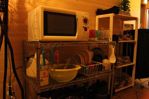 A kitchen cart with a microwave, colander, and various kitchen utensils.