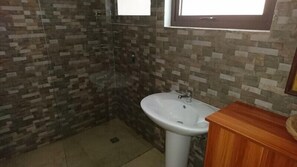 A bathroom with a tiled shower wall, a white sink, and a wooden vanity. - Royale Panorama View Apartment (Mahé Island)