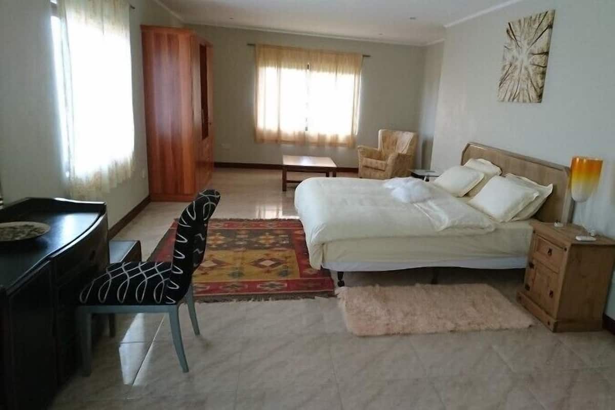 A bedroom with a bed, a desk, a chair, a nightstand, and a window with curtains.