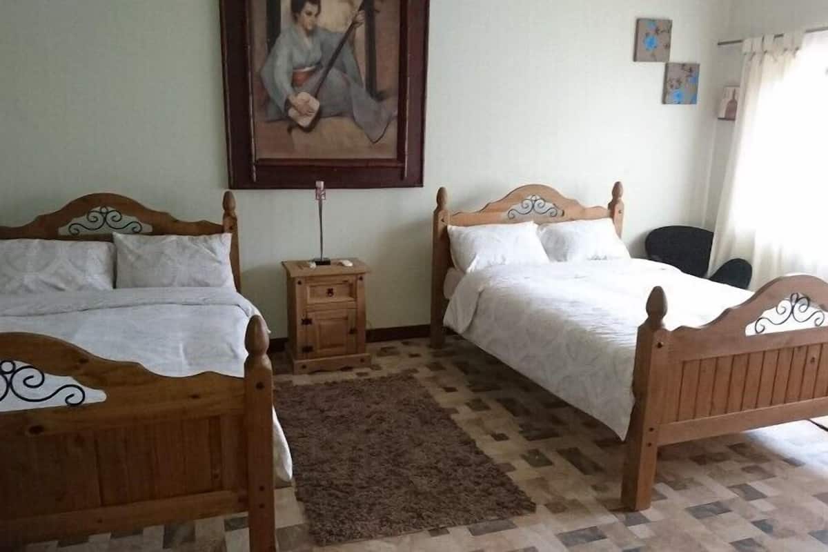 A room with two wooden beds, a small bedside table, a rug, and a painting on the wall.