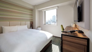 Ein Hotelzimmer mit einem großen Bett, einem Schreibtisch mit Telefon und einem an der Wand befestigten Fernseher.