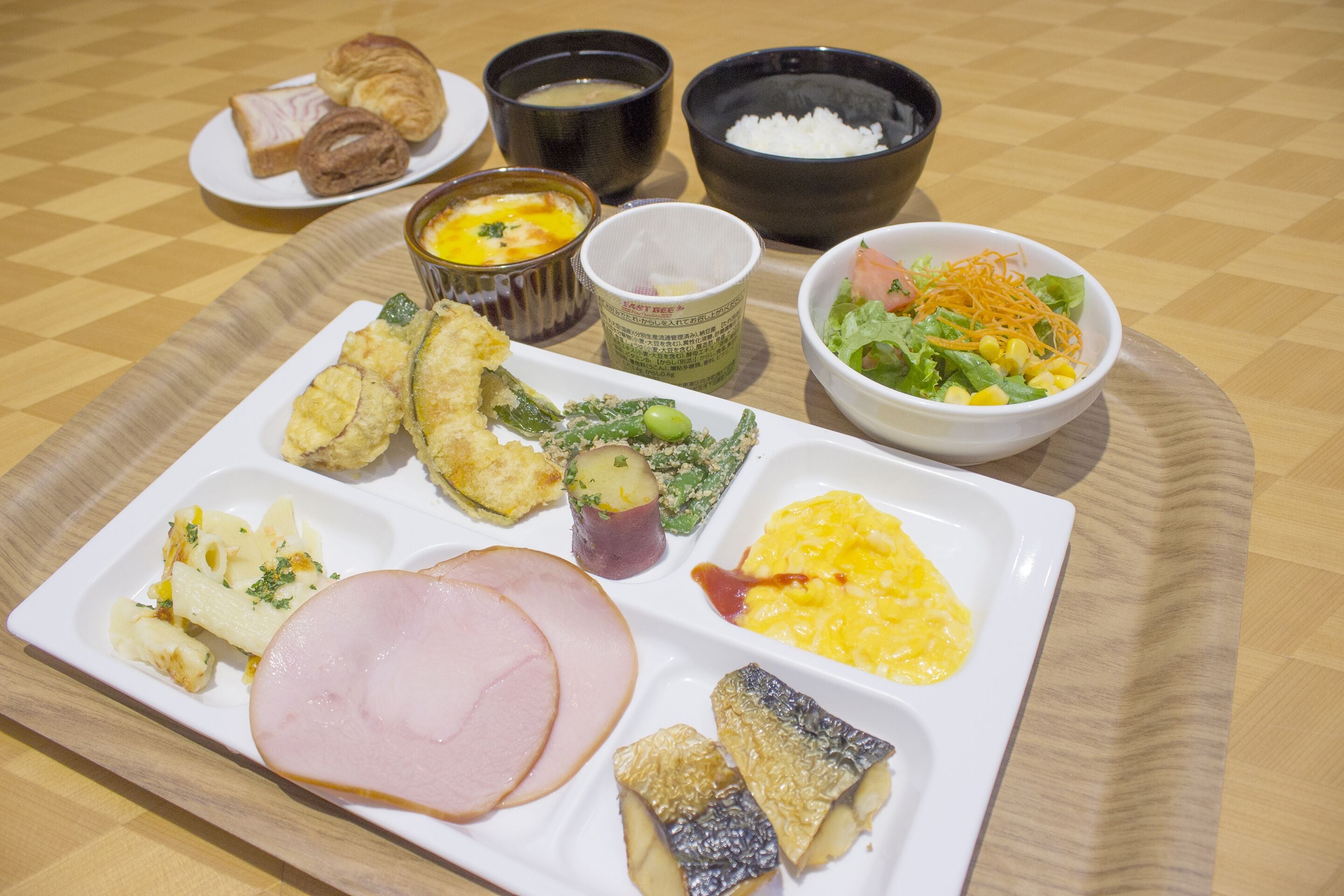 Un plateau contenant divers éléments pour le petit-déjeuner, notamment du jambon, des œufs et une salade.