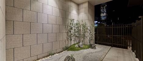 Fachada moderna de edifício com parede de azulejos, caminho de cascalho e um pequeno jardim com pedras e plantas.