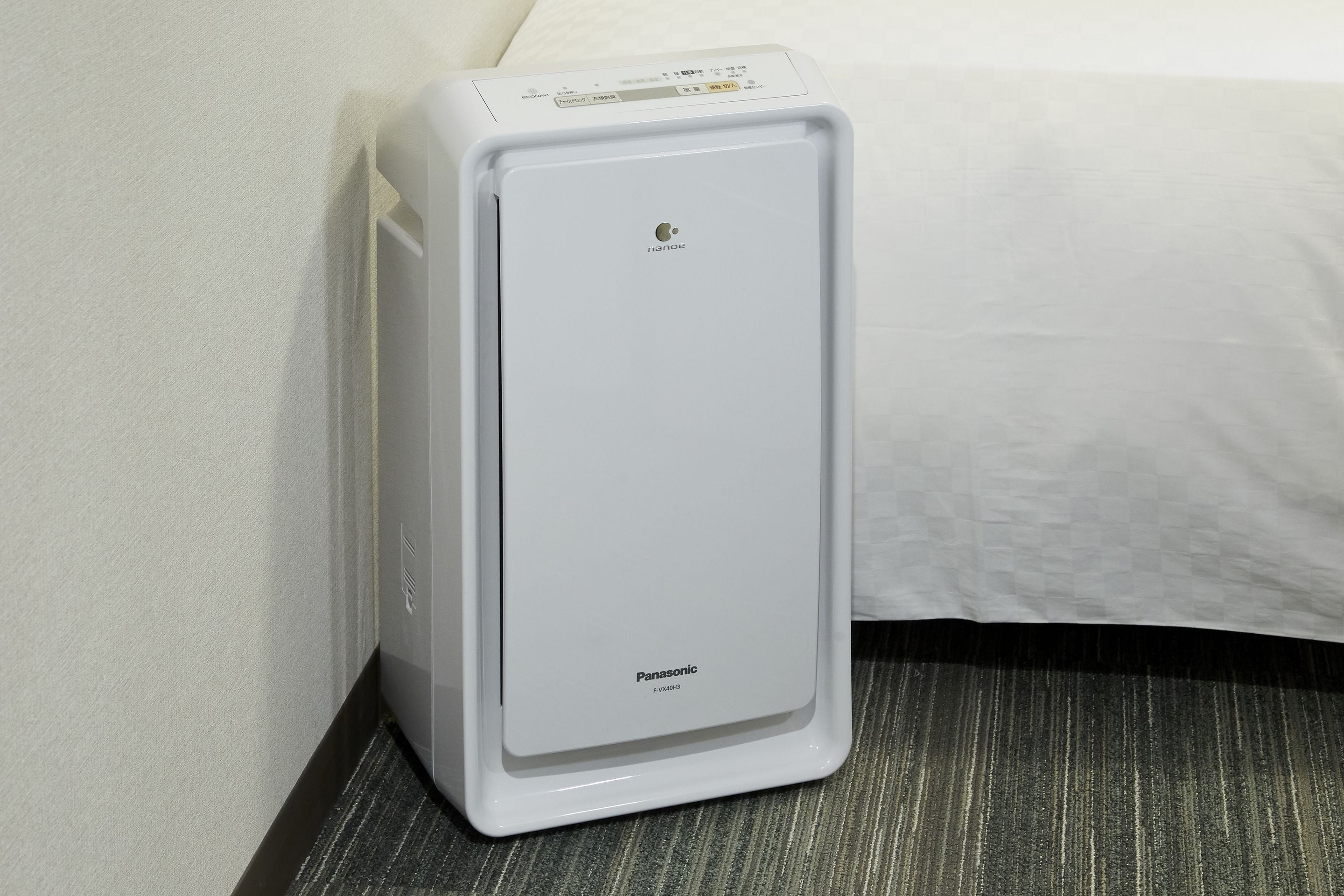 A white Panasonic air conditioner unit in a hotel room corner.