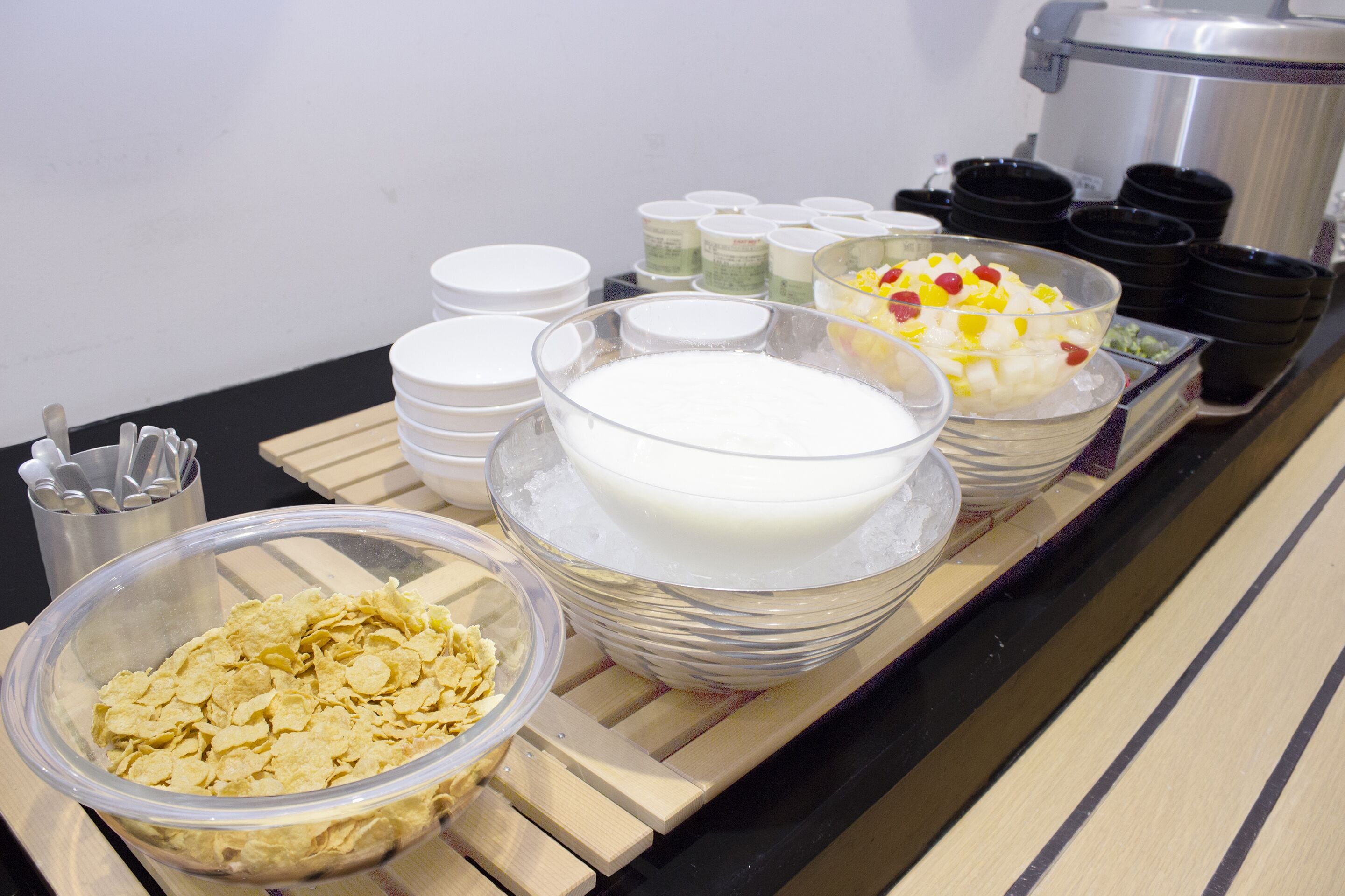 A buffet table with various food items including cereal, milk, and fruit salad.