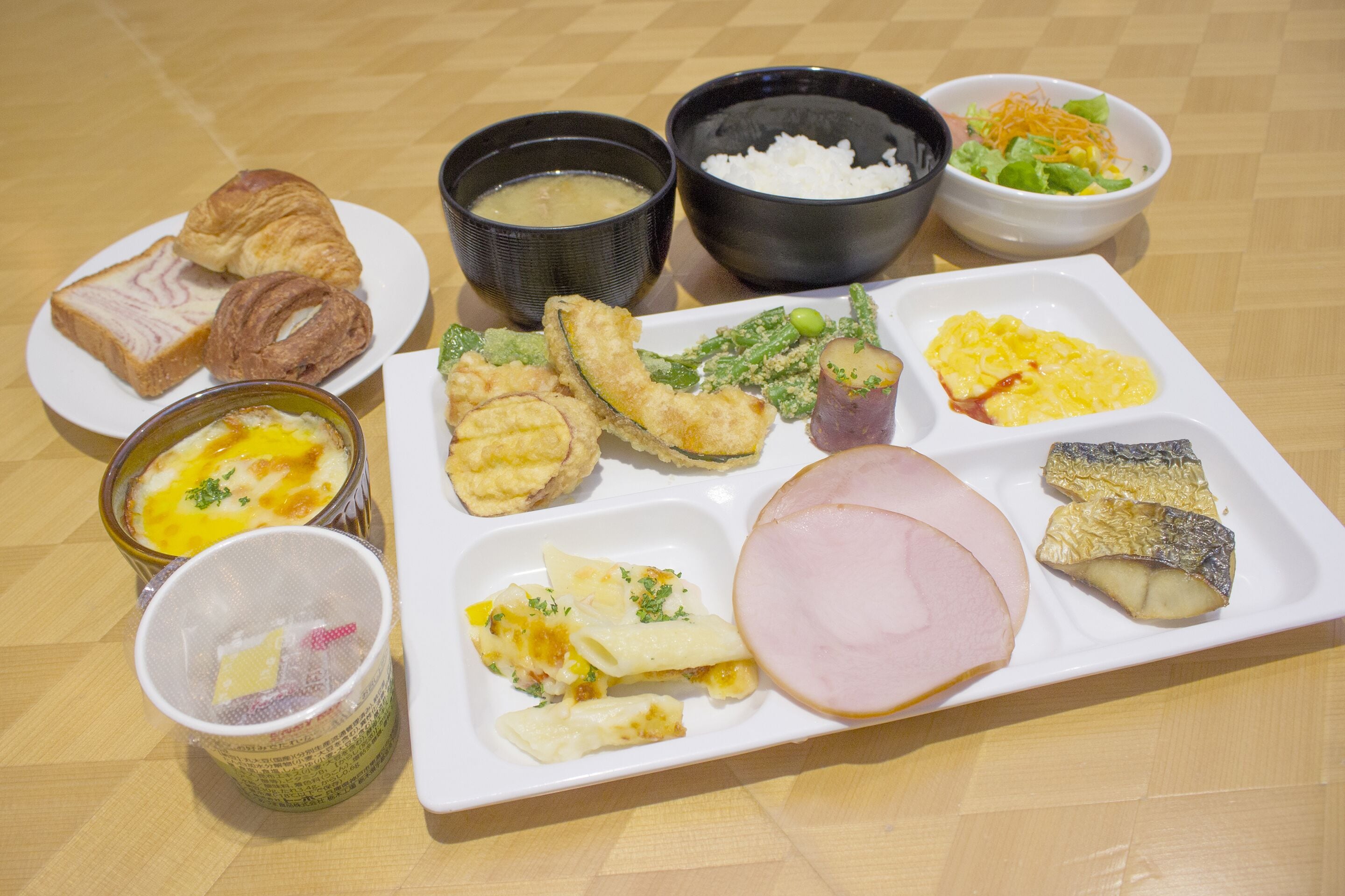 A breakfast plate with croissants, ham, fish, and various side dishes.