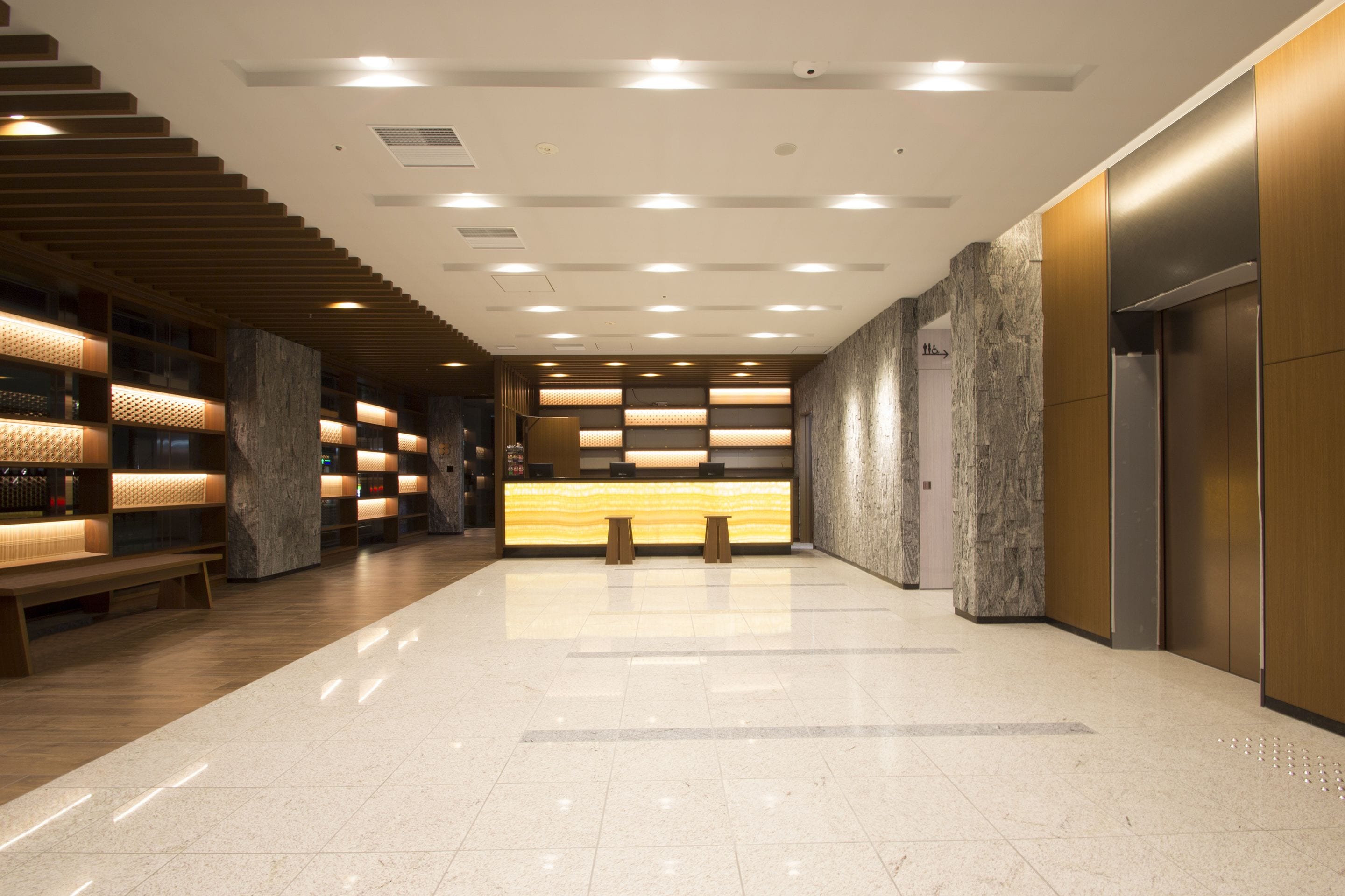 A modern lobby with a reception desk, seating area, and a staircase.