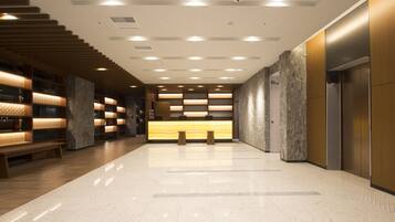 A modern lobby with a reception desk, seating area, and a staircase.