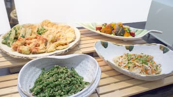 Three dishes on a wooden table: a baked dish with vegetables, a salad with mixed vegetables, and a bowl of green sauce.