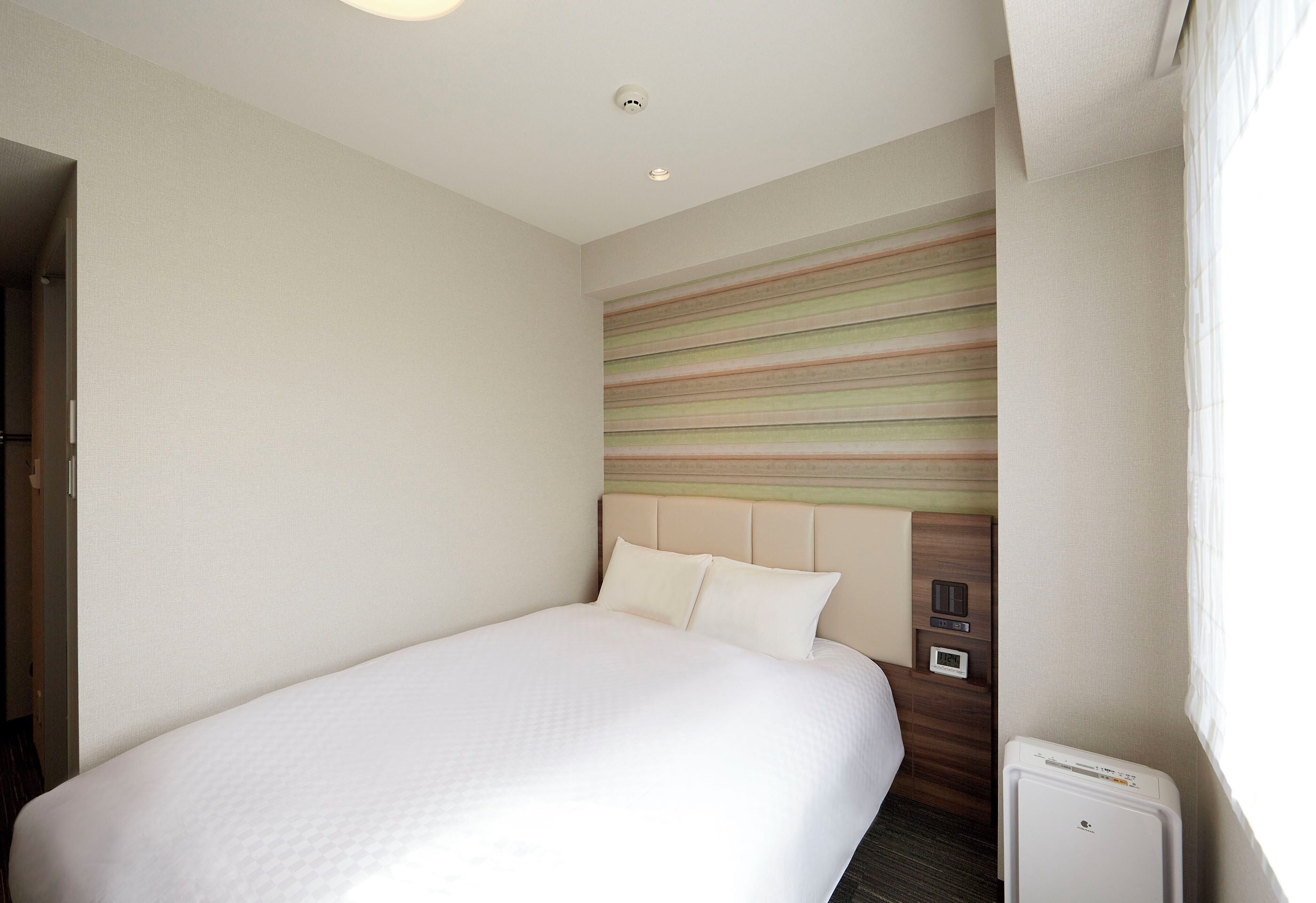 Quarto de hotel com uma cama grande, cabeceira com padrão listrado, mesa de cabeceira e um pequeno aquecedor.