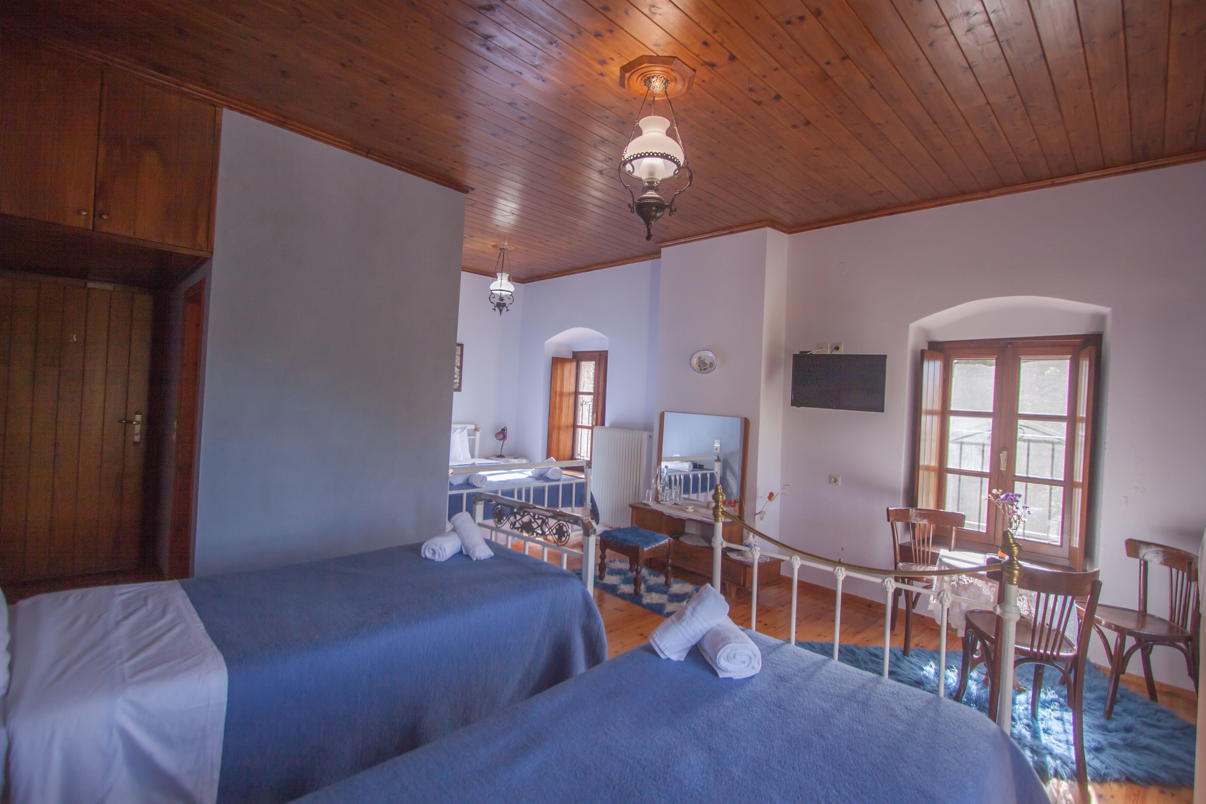 A room with two beds, wooden ceiling, a desk with a chair, and a window.