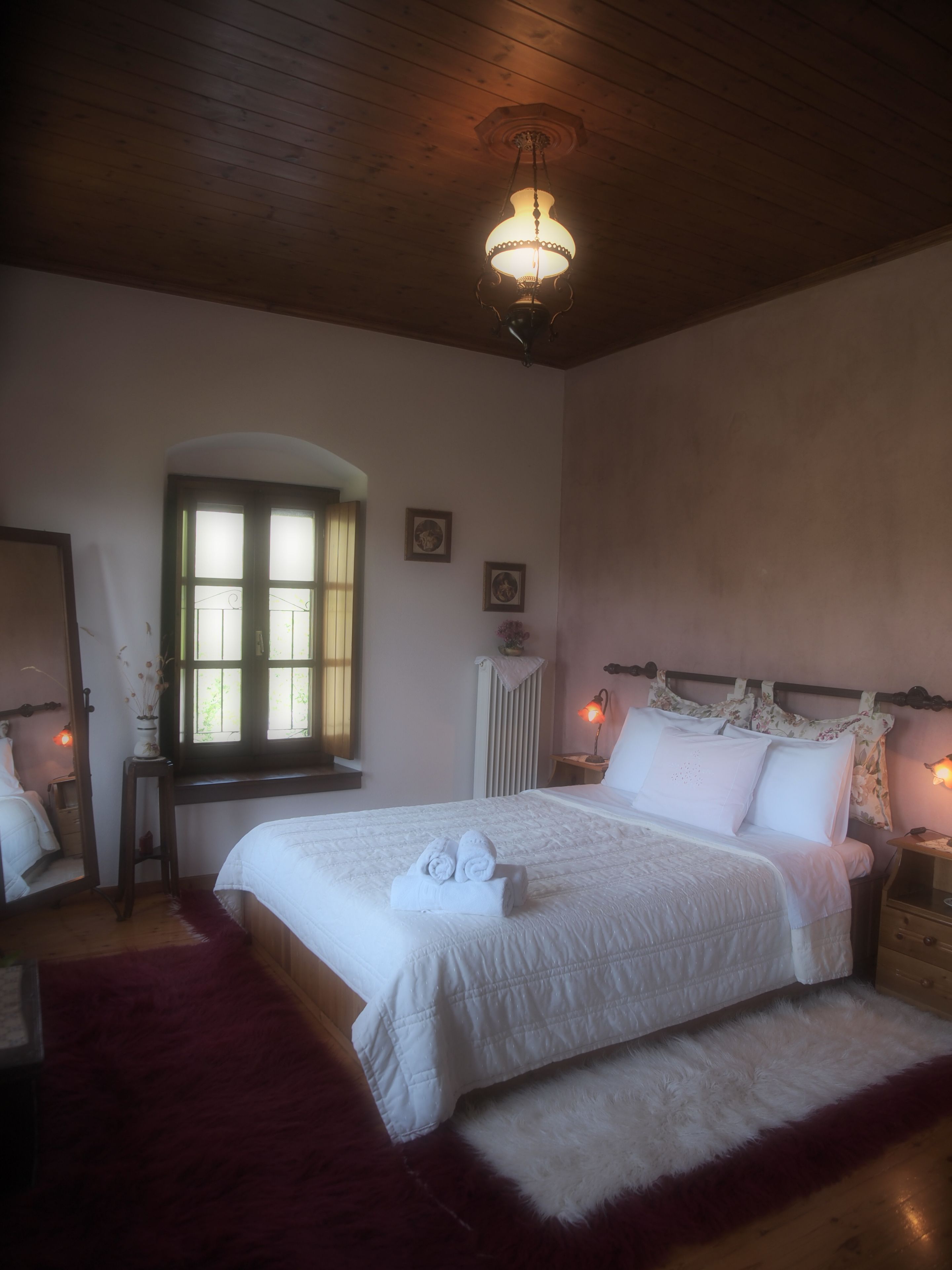 Ein Schlafzimmer mit einem großen Bett, Holzboden, einem Fenster mit Jalousien und einem Nachttisch mit Lampe.